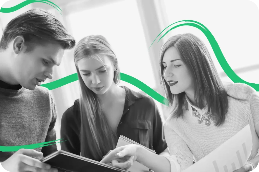 A black and white group of young business people holding papers reviewing a tablet being held