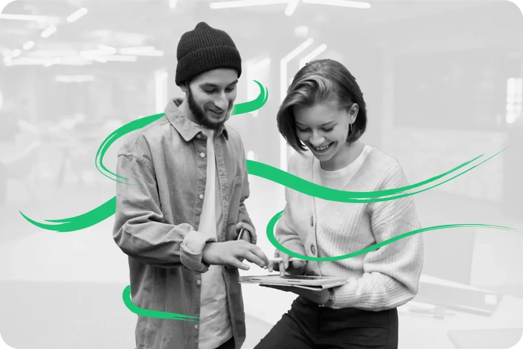 A black and white image of a man and a woman smiling while reviewing work on a tablet