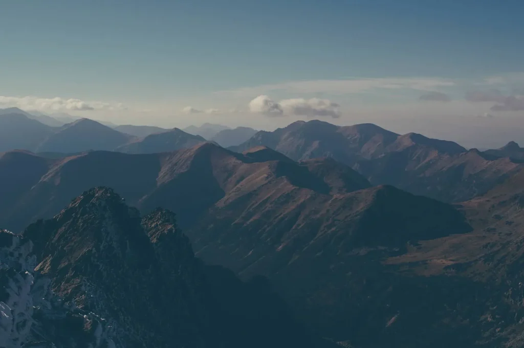 A view of mountains covered with foliage, a blue sky in the distance with a few clouds. The image has a sepia filter over it making it appear older.