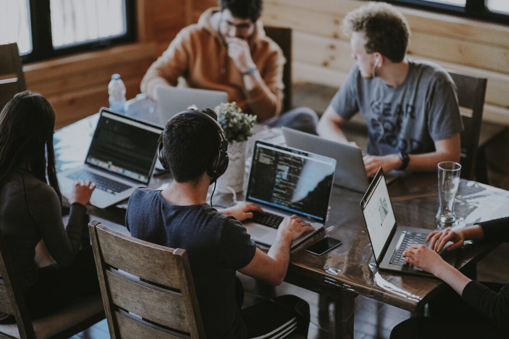 A group of people sitting around a table with laptops