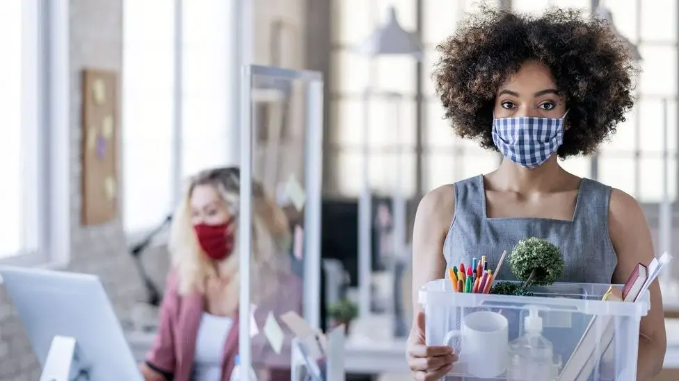 A woman wearing a face mask holding a container with items