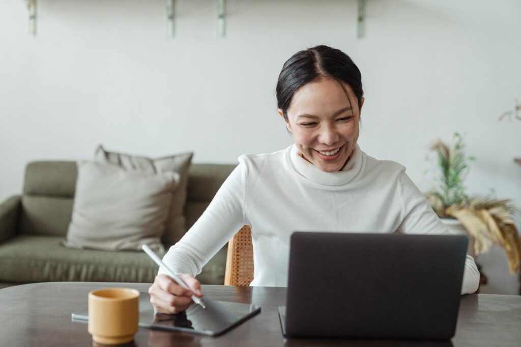 A woman sitting at a table using a laptop and a stylus