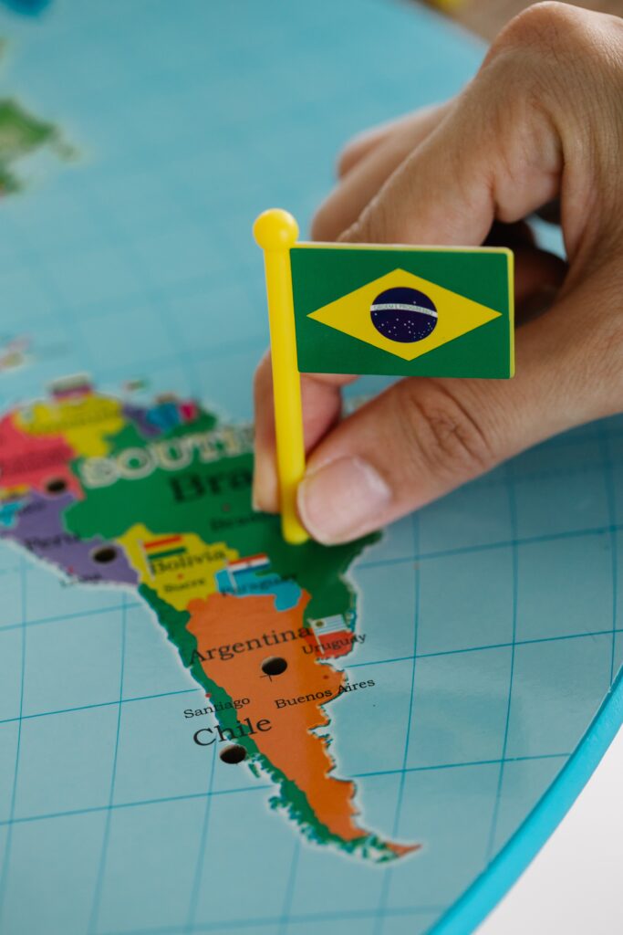 A hand holding a small Brazilian flag on a map