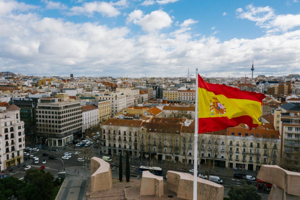 A Spanish flag on a pole with a city in the background