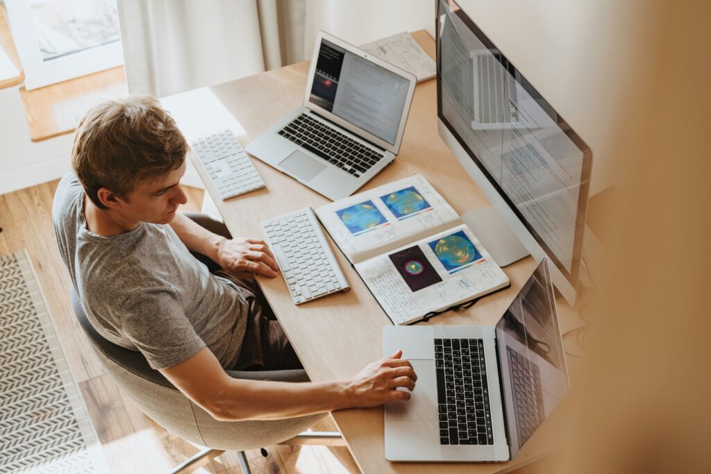 A man sitting at a desk with laptops and a book