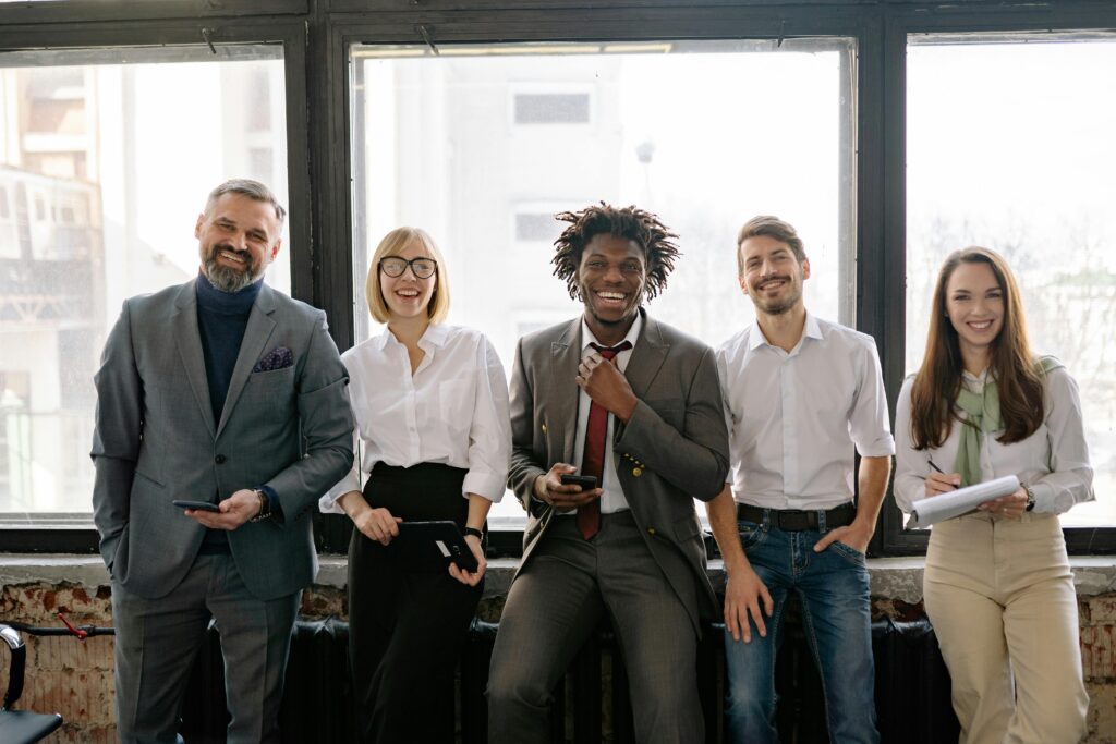 A group of people in casual business attire sitting against a radiator on a concrete wall.