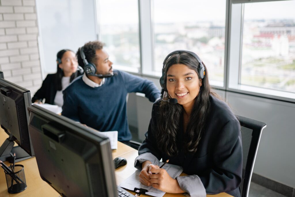 A woman wearing a headset sitting at a desk with other people in the background