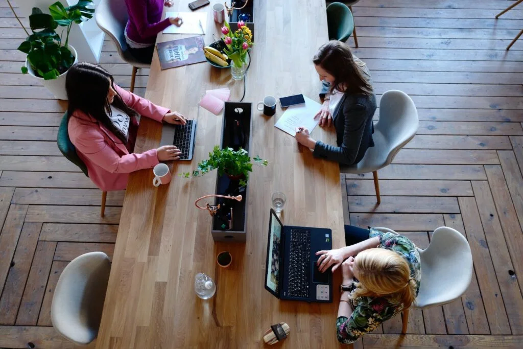 A group of women sitting at an oak table with laptops